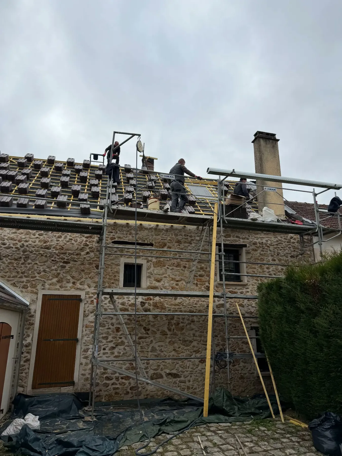 Couvreurs posant les tuiles neuves sur le liteaunage de la même maison en pierre